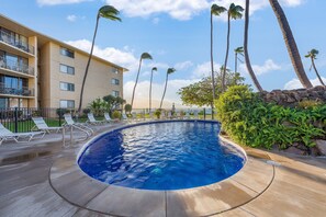 A swimming pool with lounge chairs and palm trees, surrounded by a building with balconies. - Oceanview 2BR/2BA condo with pool, AC, balcony, and beach access-Kanai A Nalu 317 (Wailuku)