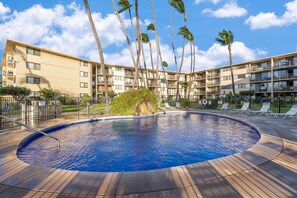 A swimming pool with a surrounding deck, palm trees, and a multi-story building with balconies. - Oceanview 2BR/2BA condo with pool, AC, balcony, and beach access-Kanai A Nalu 317 (Wailuku)