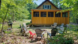 Eine Holzhütte mit Veranda, umgeben von Bäumen und Sitzgelegenheiten im Freien.