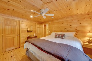 A wooden cabin bedroom with a bed, a ceiling fan, and a nightstand. - North Conway: Updated 3BR Cabin Sleeps 9, Fire Pit (North Conway)