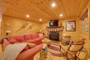 A cozy log cabin interior with a fireplace, a television mounted above it, and a red sofa. - North Conway: Updated 3BR Cabin Sleeps 9, Fire Pit (North Conway)