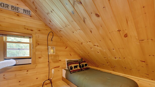 Ein kleines Zimmer mit einem Einzelbett, Holzwänden und einer schrägen Decke.