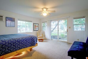 Ein Schlafzimmer mit Bett, Stuhl, Deckenventilator und großen Fenstern.
