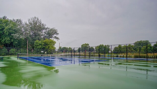 Una cancha de tenis con red, rodeada por una valla y árboles.