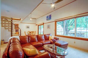 A spacious living room with a brown leather sofa, a glass coffee table, and a large window offering a view of the outdoors. - West Okoboji Waterfront Home w/ Private Dock (Milford)