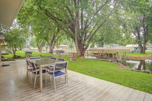 Eine Terrasse im Freien mit Tisch und Stühlen, umgeben von Bäumen und einem kleinen Teich.