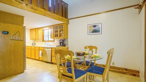 Un comedor con una mesa de vidrio, sillas de madera y una cocina al fondo.
