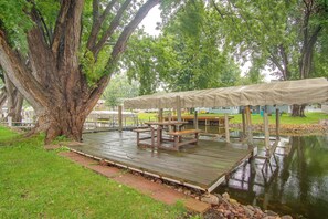 Eine Holzterrasse mit überdachtem Picknicktisch und Bänken, umgeben von einem Teich und Bäumen.