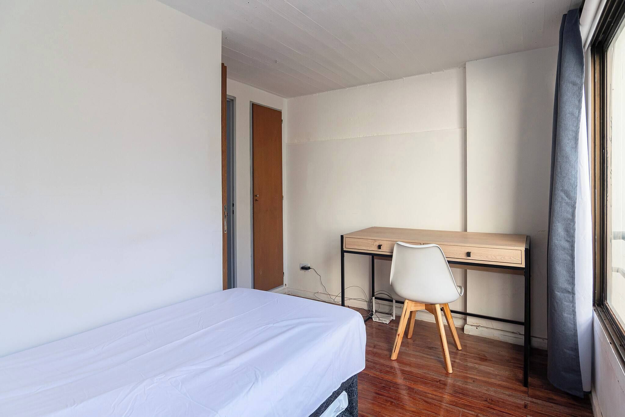 Una habitación pequeña y poco amoblada con una cama individual, un escritorio y una silla.