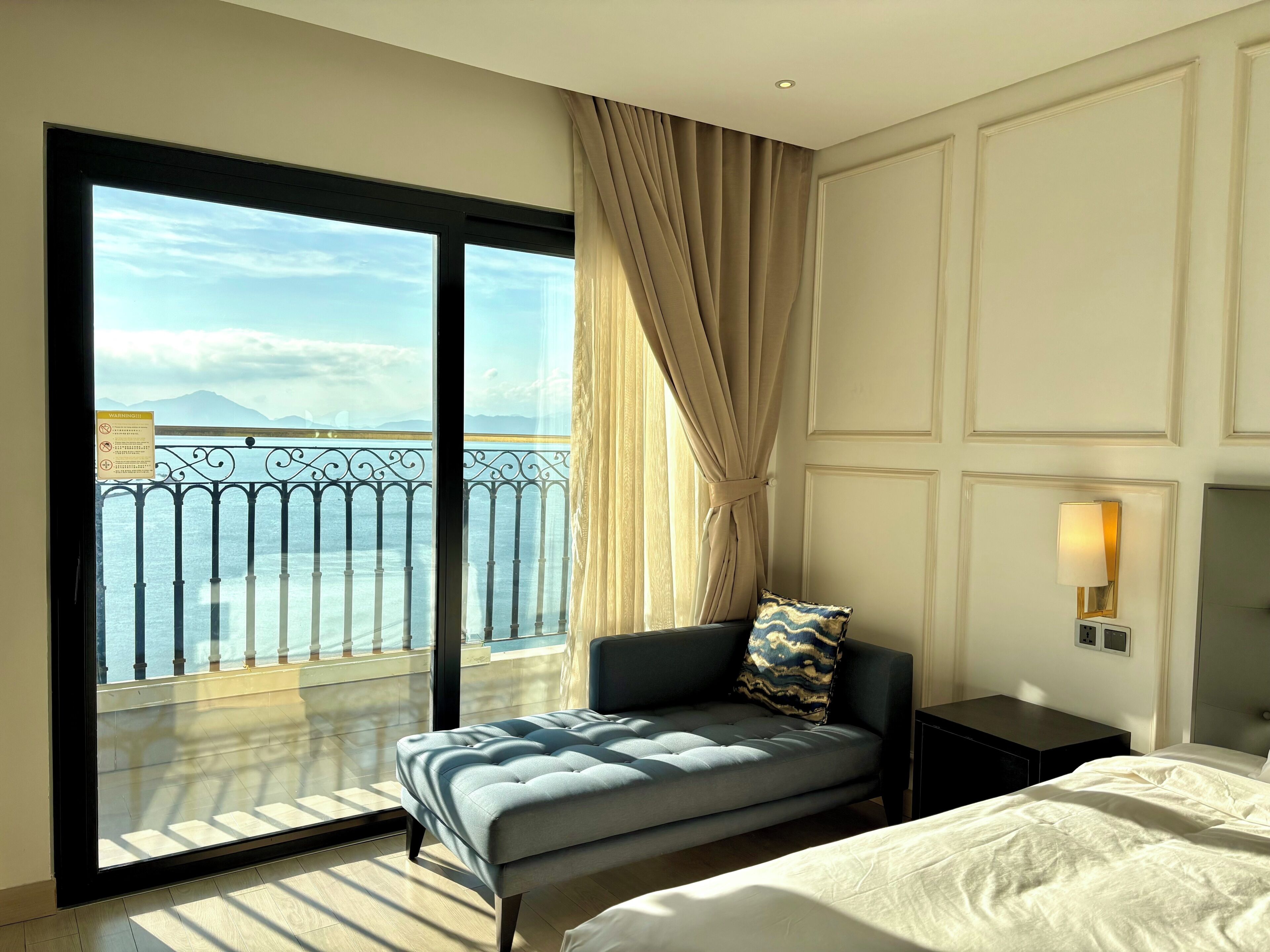 Ein Hotelzimmer mit einem großen Balkon, einem Bett, einem Nachttisch und einer Lampe.