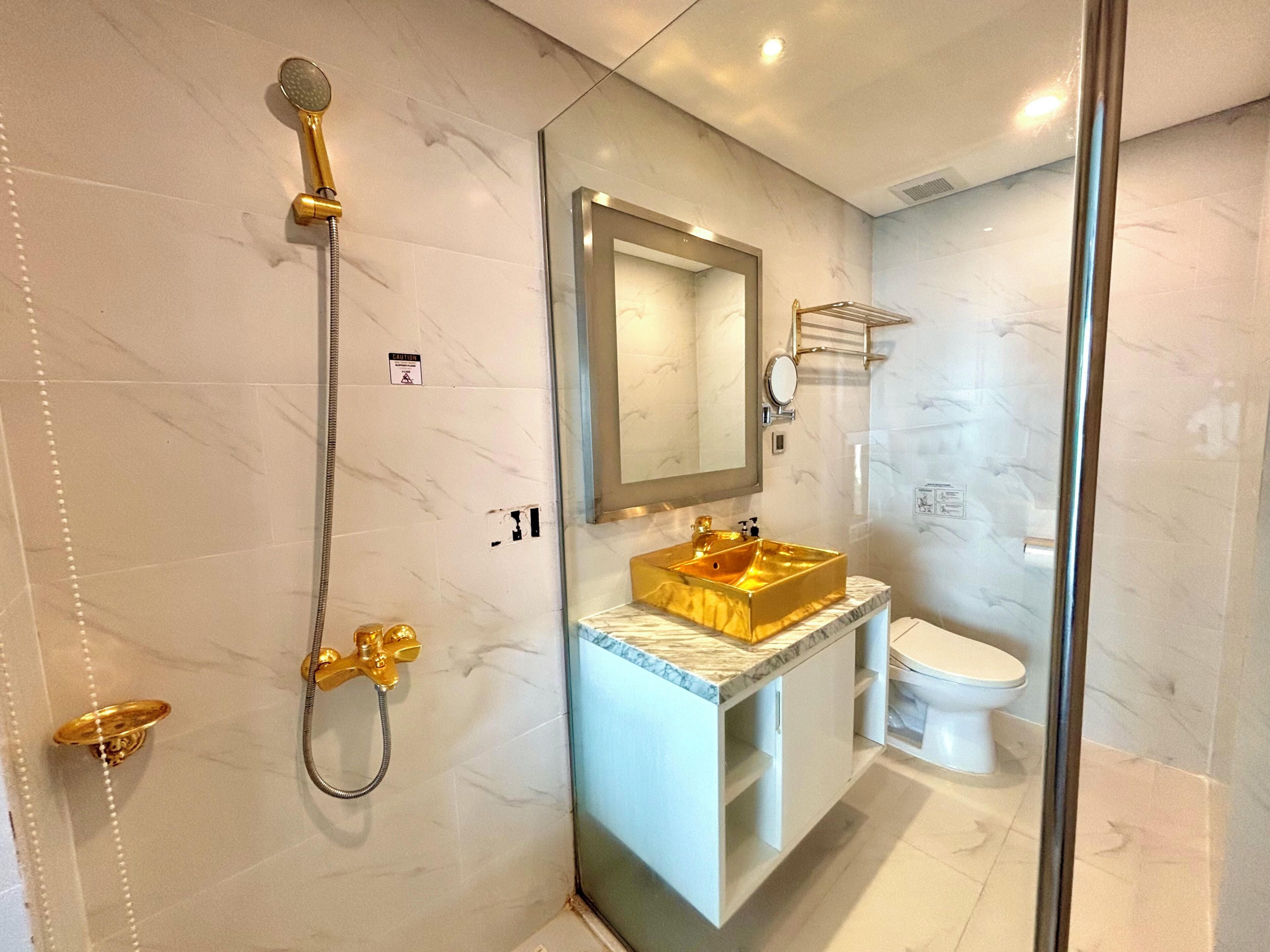 Casa de banho com lavatório dourado, chuveiro e sanita.