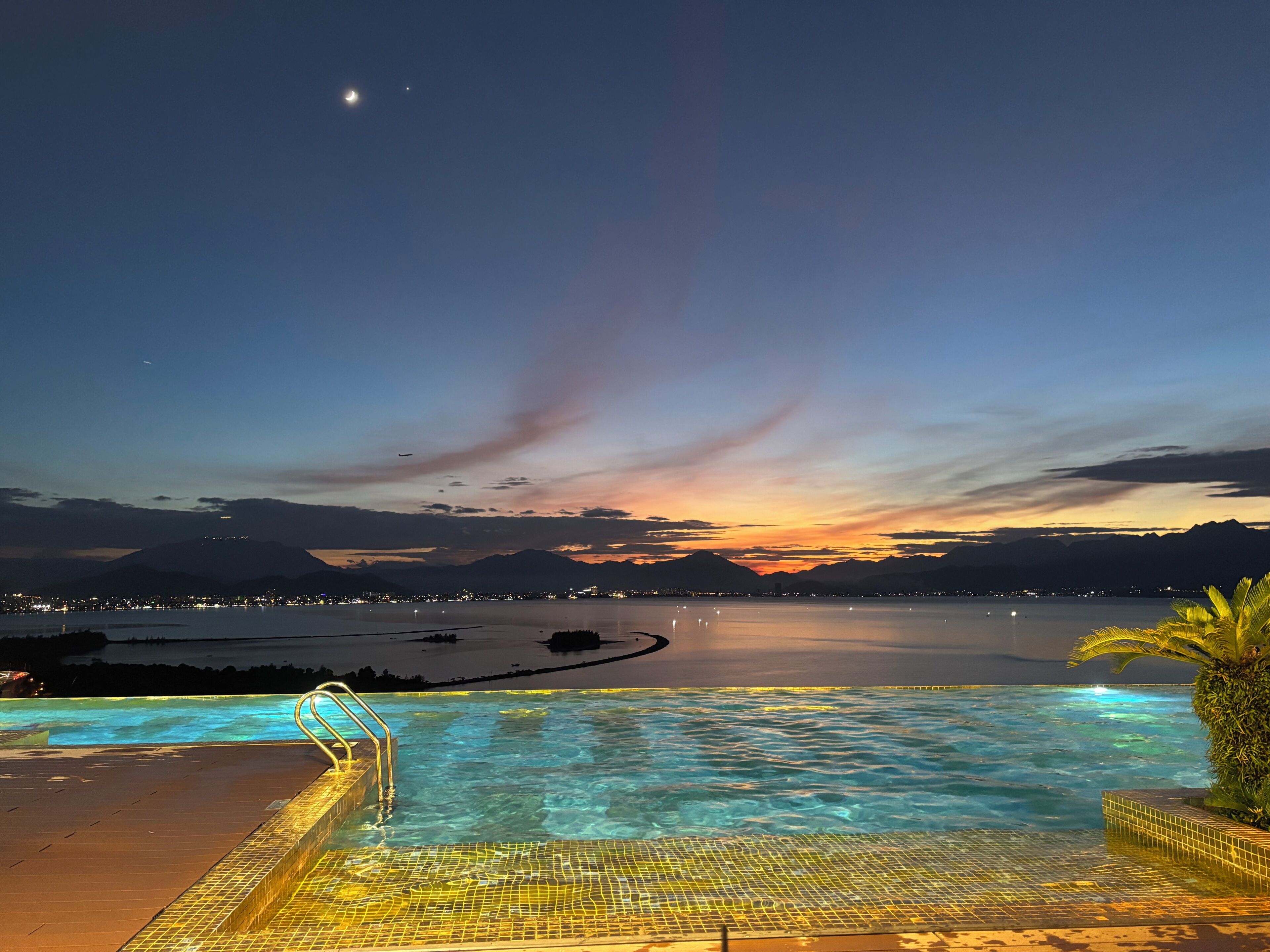 A swimming pool with a view of a sunset over a body of water and mountains.