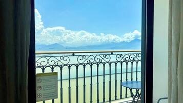 A balcony with a view of the sea and mountains, a warning sign, and a small table.