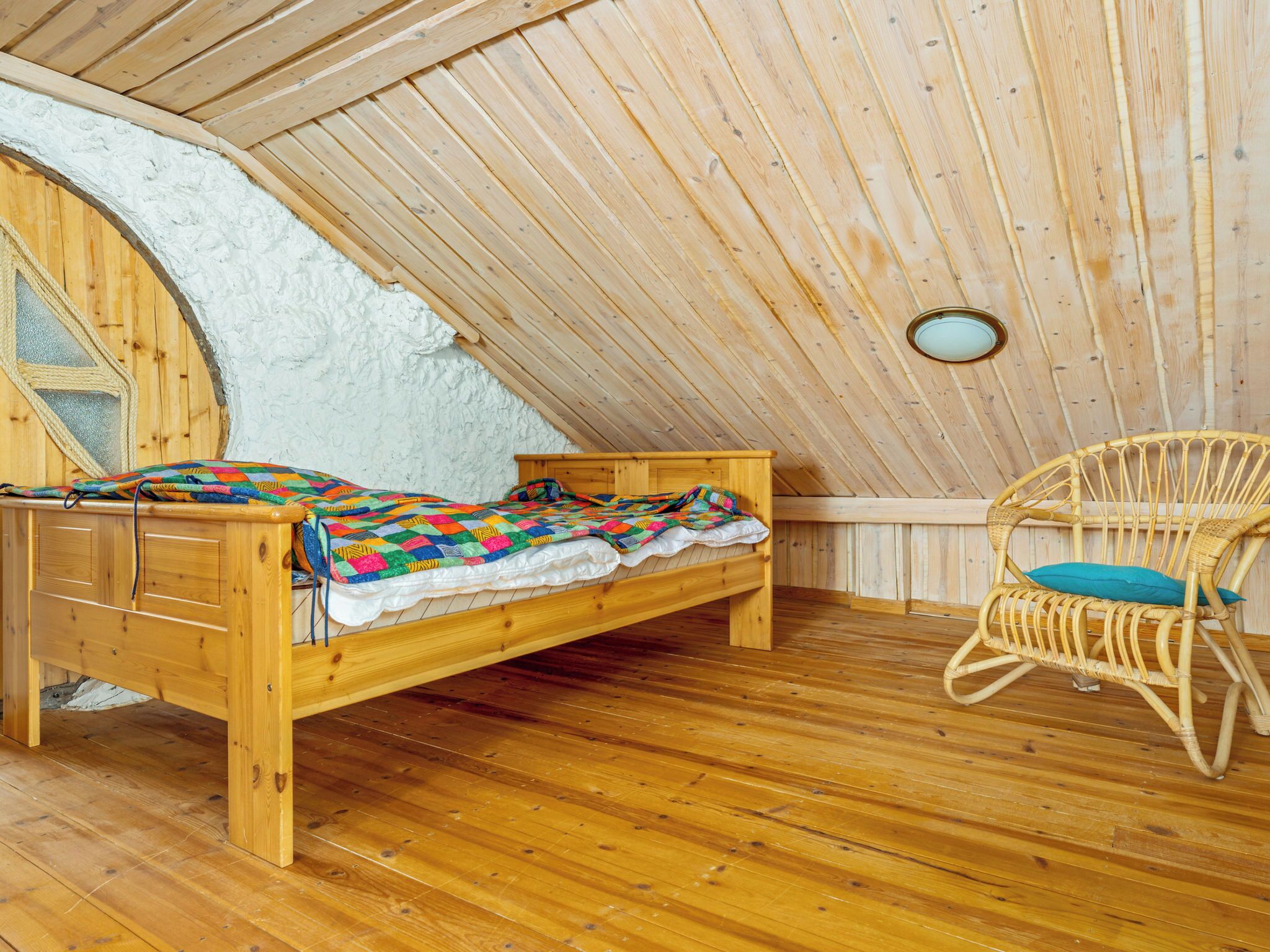 A wooden loft bedroom with a bed, a chair, and a small window.