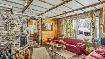 A cozy cabin interior with a stone wall, wooden beams, a red leather sofa, and a fireplace.