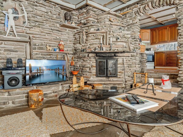 A stone fireplace, a television, and a kitchen area with wooden cabinets.
