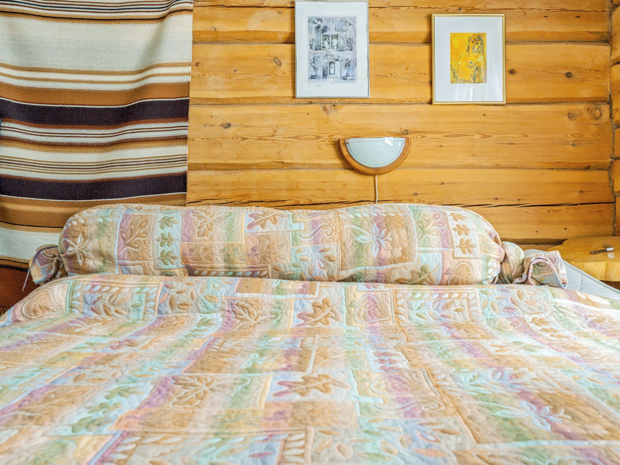 A bed with a patterned quilt, a wooden headboard, and a nightstand with a lamp.