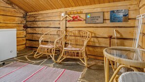 A log cabin interior with two wicker chairs, a glass table, and a refrigerator.
