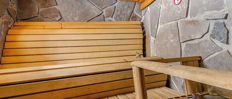 Un sauna avec des bancs en bois et un mur en pierre.