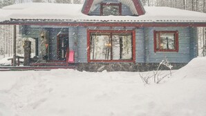 A snow-covered cabin with a gabled roof, large windows, and a visible door.