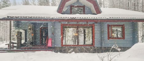 Una baita imbiancata dalla neve con tetto a due falde, ampie finestre e una porta ben visibile.
