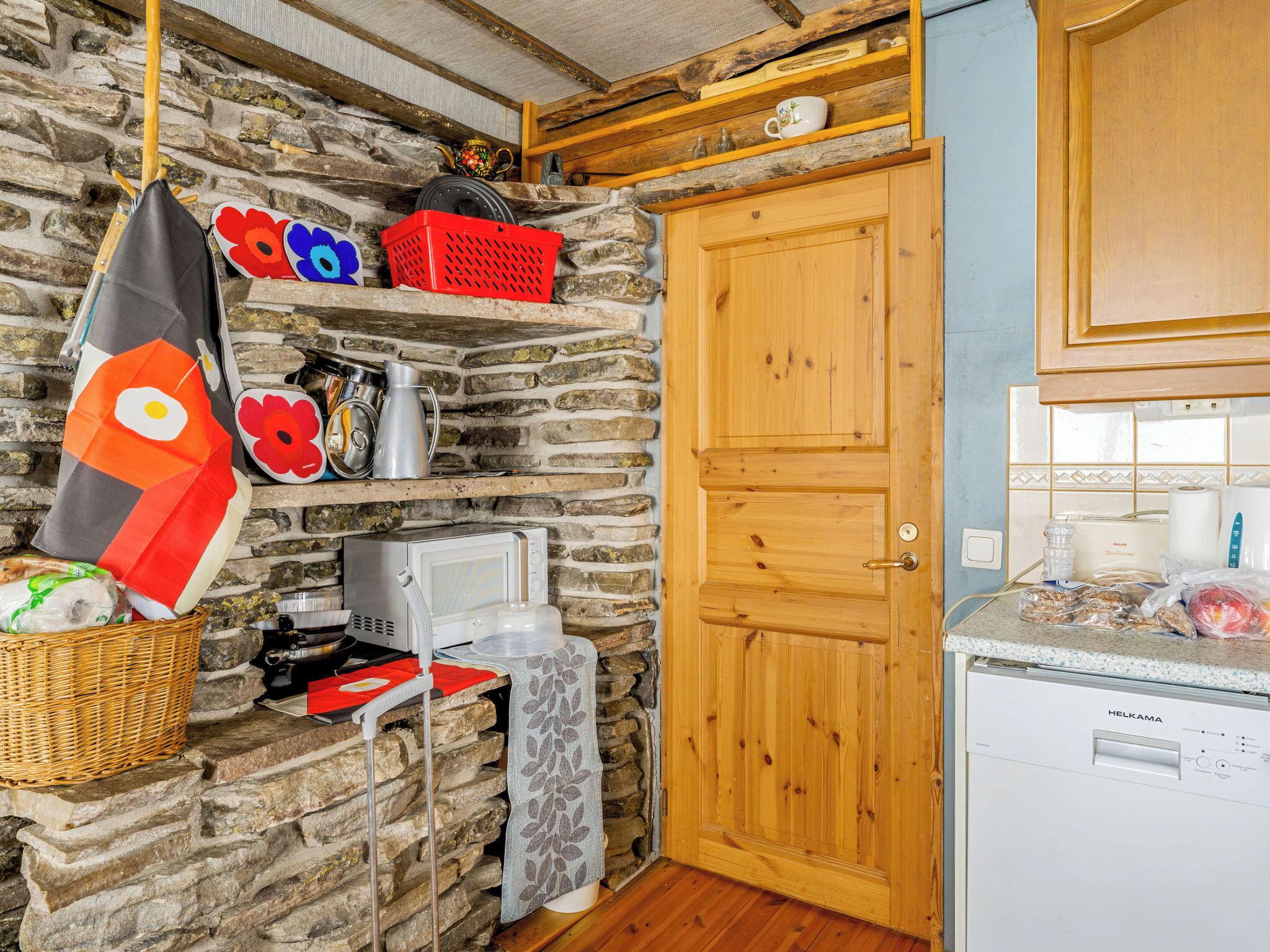 Una cocina rústica con pared de piedra, armarios de madera, microondas y lavadora.