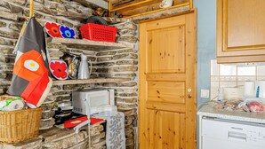 A rustic kitchen with a stone wall, wooden cabinets, a microwave, and a washing machine.