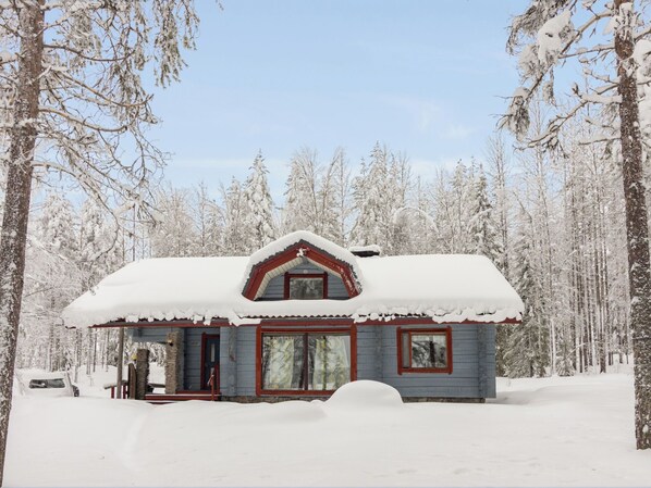 Una cabaña de madera con techo nevado, rodeada de un bosque.