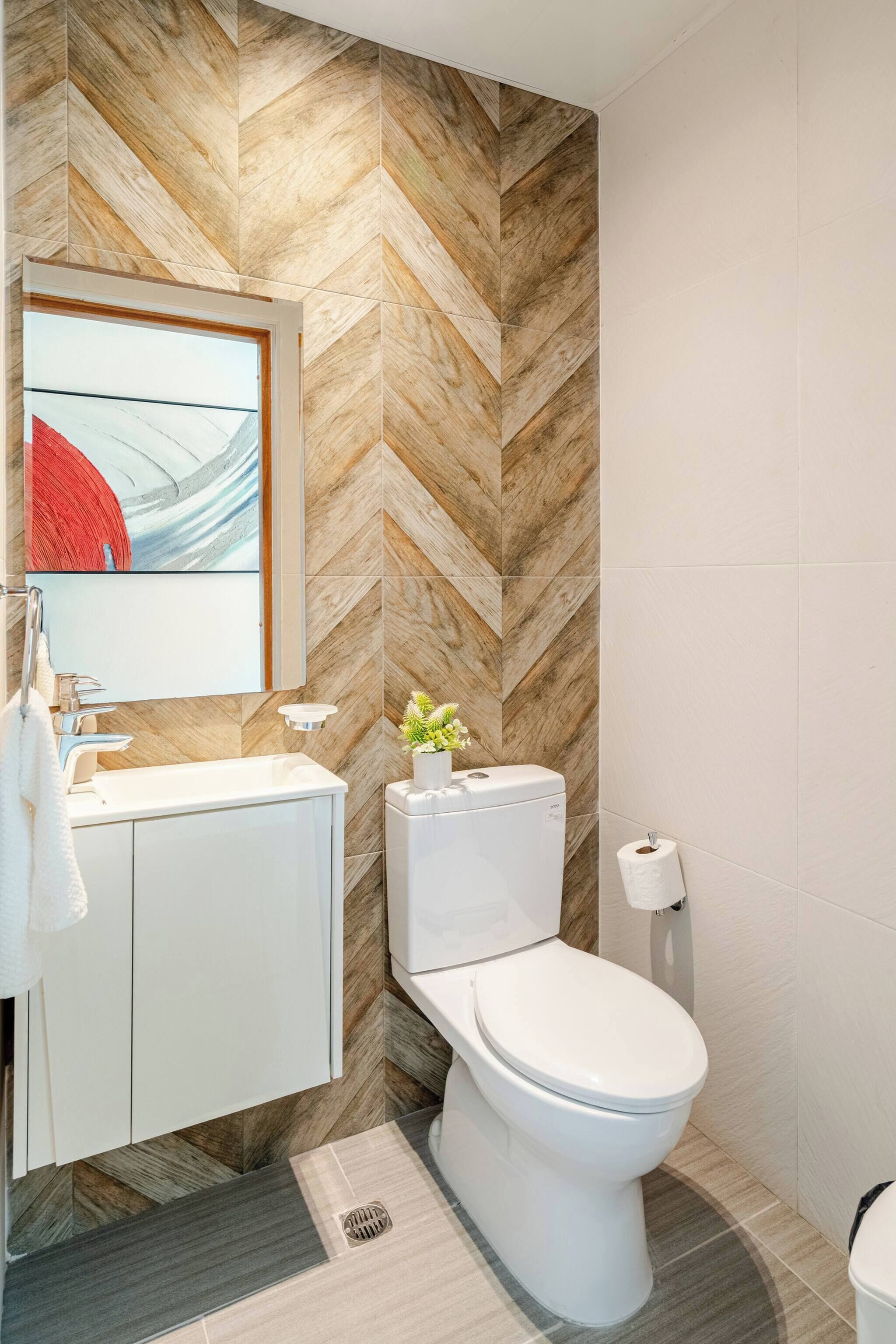 A modern bathroom with a herringbone patterned wall, a white toilet, a sink with a mirror, and a towel hanging on the wall.