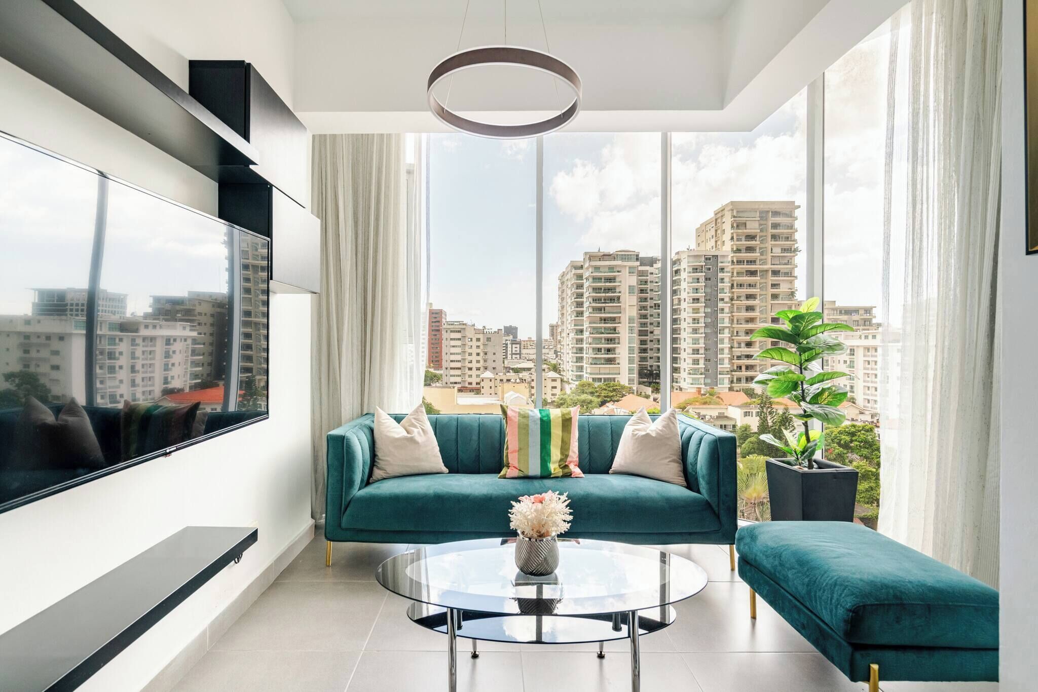 Ein modernes Wohnzimmer mit einem türkisfarbenen Sofa, einem Glastisch und einem großen Fenster mit Blick auf die Stadt.