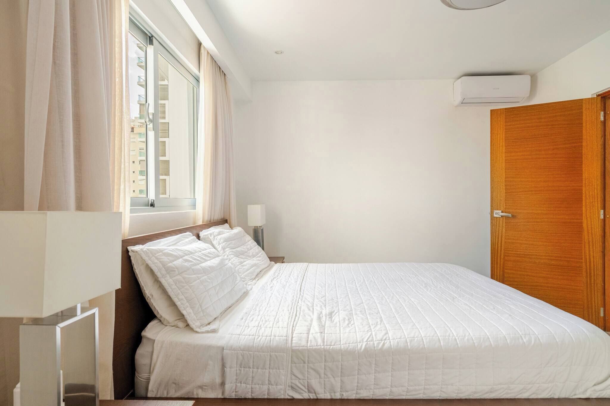 Une chambre à coucher avec un lit, une fenêtre avec des rideaux, une table de chevet avec une lampe et une armoire.