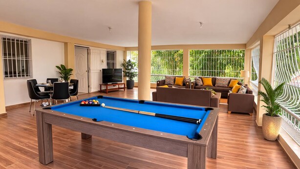 A pool table in a spacious room with a sofa set, a television, and large windows.