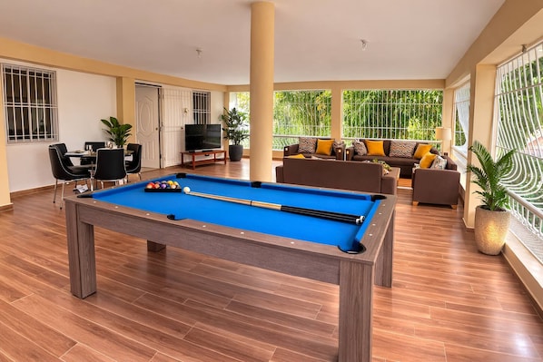 A pool table in a spacious room with a sofa set, a television, and large windows.