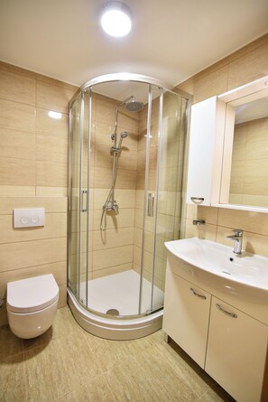Un baño moderno con ducha acristalada, inodoro blanco y tocador con espejo.