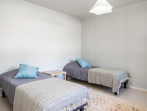 A bedroom with two single beds, a small bedside table, a patterned rug, and a hanging light fixture.