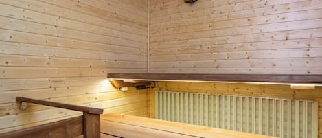 A sauna with wooden walls and benches, a visible ceiling vent, and a radiator.