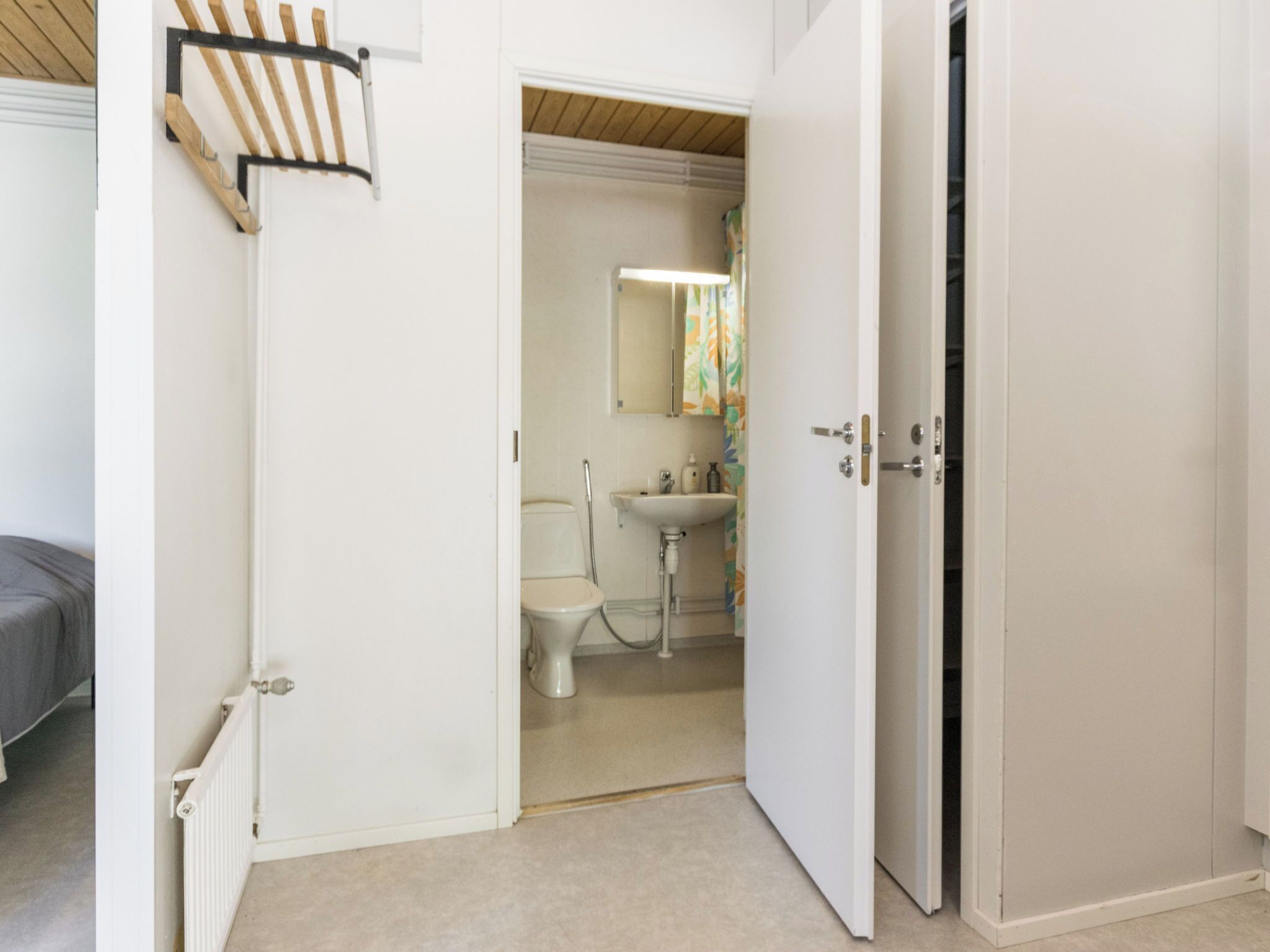 Et værelse med en seng, en radiator, en hvid dør og et badeværelse med toilet og vask.