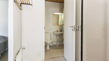 Et værelse med en seng, en radiator, en hvid dør og et badeværelse med toilet og vask.