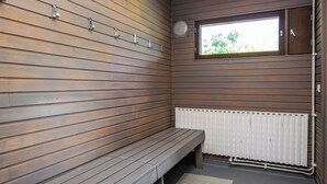 A bench in a room with wooden panel walls, a window, and a white radiator.