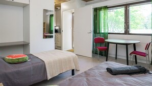 A bedroom with a bed, a small table, and chairs. There is a window with curtains and a view of trees.