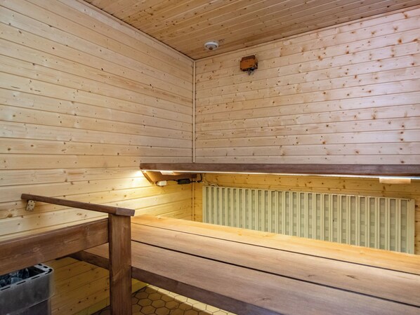 A sauna with wooden walls and benches, a visible ceiling vent, and a radiator.