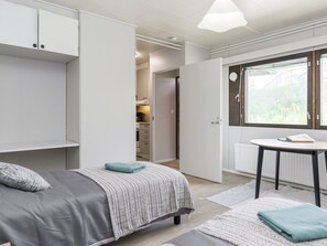 A bedroom with a bed, a small table, a window, and a door leading to a bathroom.