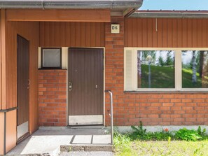 A two-story building with a brown wooden facade, a brown door, and a window with a view of greenery.