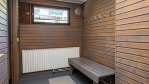 A sauna room with wooden walls, a bench, a window, and a radiator.
