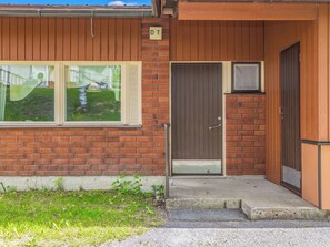 A two-story building with a brick facade, a wooden door, and a window with a view of a grassy area. - Heinävesi homes d7 by Interhome (Heinävesi)