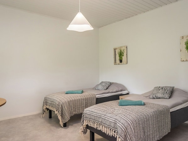 A simple, clean room with two single beds, a hanging light fixture, and a small wall decoration.