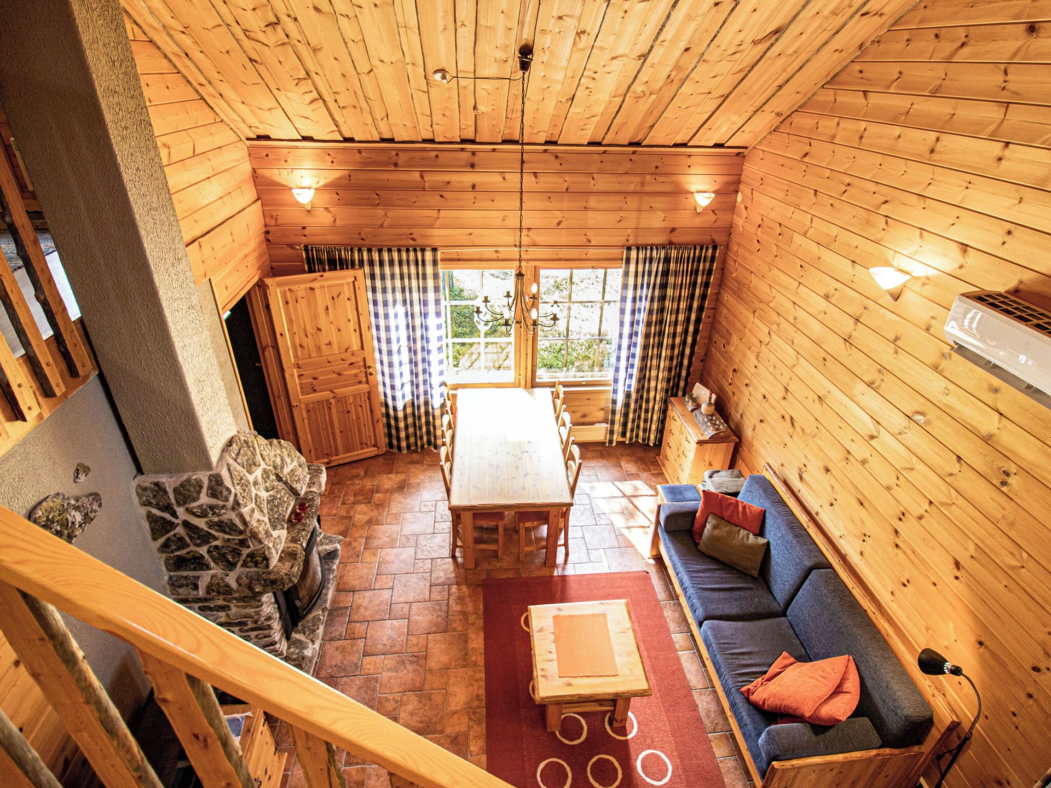 A wooden interior with a stone fireplace, a dining table, and a sofa.