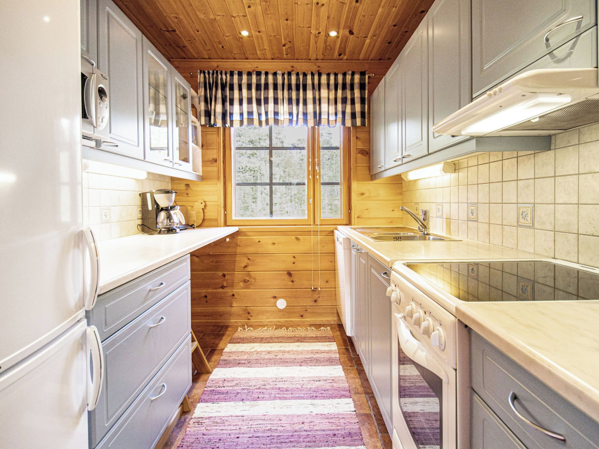 A compact kitchen with wooden cabinets, a built-in oven, and a window with curtains.
