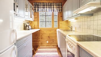 A compact kitchen with wooden cabinets, a built-in oven, and a window with curtains.