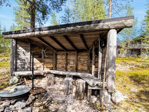 Una cabana de fusta rústica amb una panxa a l'exterior, envoltada de pedres i arbres.